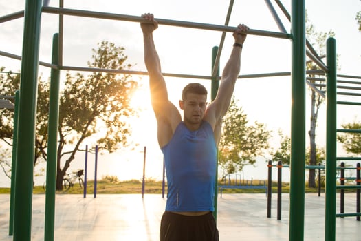 Muscular man doing pull-ups on horizontal bar, training of strongman on outdoor park gym in the morning. photo