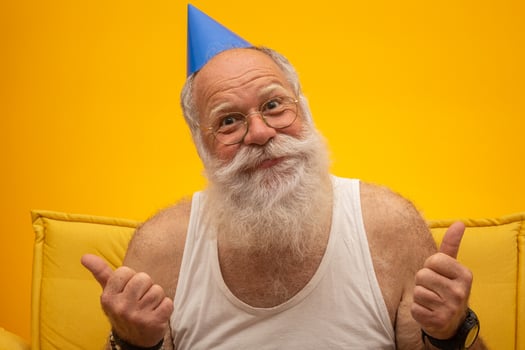 Positive elderly man in party hat smiling to camera, birthday celebration photo
