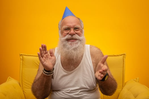 Positive elderly man in party hat smiling to camera, birthday celebration photo