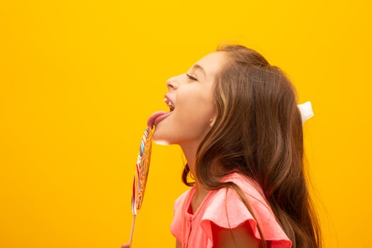 The child is holding a lollipop. Childish joy is sweetness. Little girl on yellow background. photo