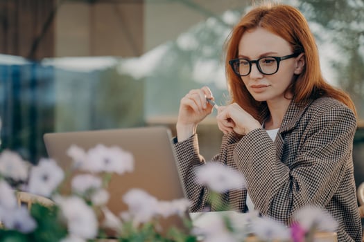 Young focused red-haired business woman works online at outdoor cafe photo