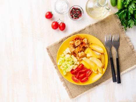 baked potato slices and turkey stew with vegetables on bright yellow plate, on white rustic background, top view, overhead, copy space photo