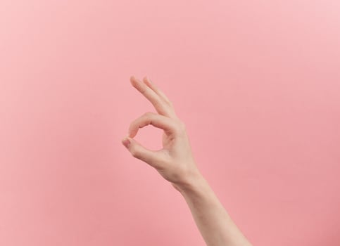 Woman hand shows ok symbol on pink pastel background with copy space photo