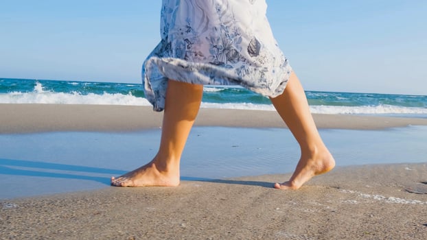 Young beautiful woman dressed in a white dress walk barefoot on the summer beach photo