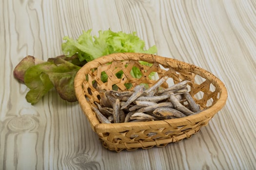 Dries anchovy in a basket on wooden background photo