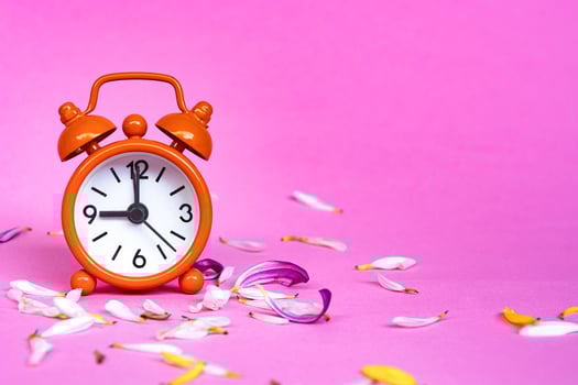 Orange alarm clock set at 9 o'clock isolated with flower petals. photo