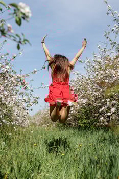 Young caucasian woman in red dress enjoying the flowering of an apple trees, jumping photo