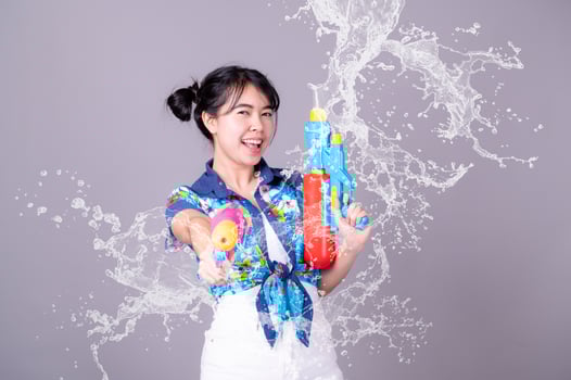 A beautiful Asian woman shows a gesture while holding a plastic water gun during the Songkran festival photo