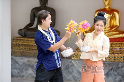 Young Thai men and women in traditional Thai dress hold flowers splashing water for fun at the Songkran water festival photo