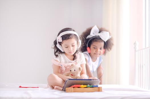 A cute Asian girl and an African kid friend are using a tablet to play games and have fun learning in the room photo