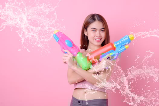 A beautiful Asian woman shows a gesture while holding a plastic water gun during the Songkran festival photo