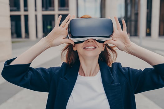 Young smiling redhead female entrepreneur testing portable VR goggles on city street photo