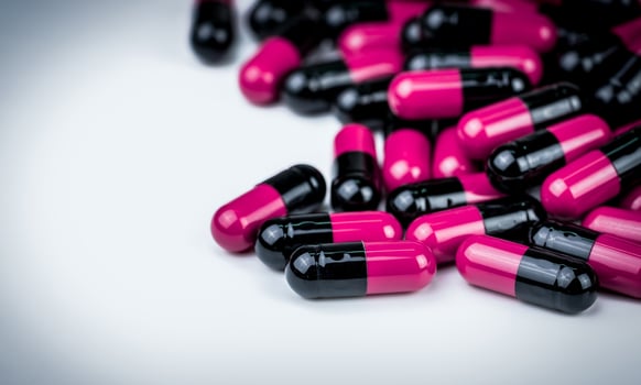 Pink-black capsule pills on white table. Antibiotics drug resistance. Global healthcare. Antimicrobial capsule pills. Pharmacy background. Antibiotic drug use with reasonable. Pharmaceutical industry. photo