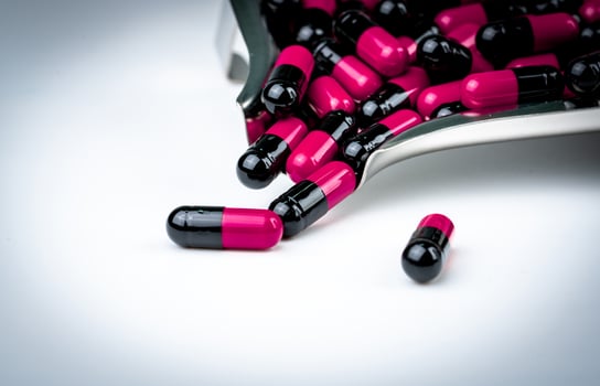 Pink-black capsule pills on drug tray. Antibiotics drug resistance. Global healthcare. Antimicrobial capsule pills. Pharmacy background. Antibiotic drug use with reasonable. Pharmaceutical industry. photo