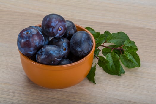 Fresh plums in a bowl on wooden background photo