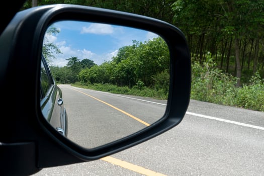 Inside view of mirrors wing. Rear view of a gray car with asphalt road and green trees in the daytime. Clear traffic in rural areas. photo