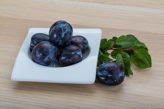 Fresh plums in a bowl on wooden background photo