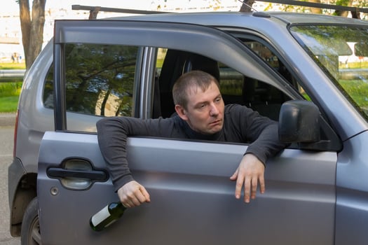 Drunk driver with a bottle of alcohol falls out of the door of his own car photo