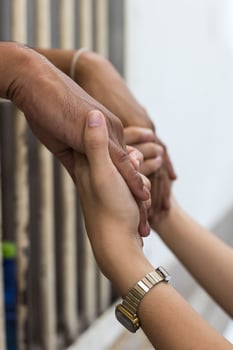Woman holding the hand of a male prisoner in a white cage. photo