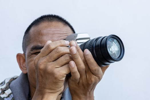 Isolated close-up of a Thai man holding a large DSLR film camera with a black zoom lens. photo