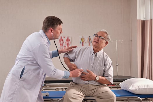 Caucasian male doctor in uniform health checks illness senior patient with stethoscope, painful stomach ache in bed of emergency room at hospital ward, elderly medical clinic examination consultant. photo