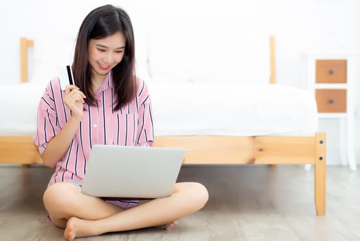 Beautiful of portrait young asian woman sitting users credit card with laptop, content girl shopping online and payment with notebook computer on bed at bedroom, lifestyle concept. photo