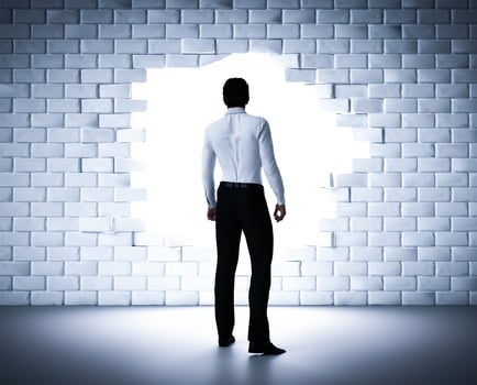 Businessman standing next to a hole in a brick wall. Light coming from outside photo
