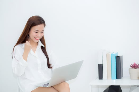 Beautiful of portrait happy young asian woman using laptop work with success on chair in the home, girl and notebook shopping online with glad, communication concept. photo