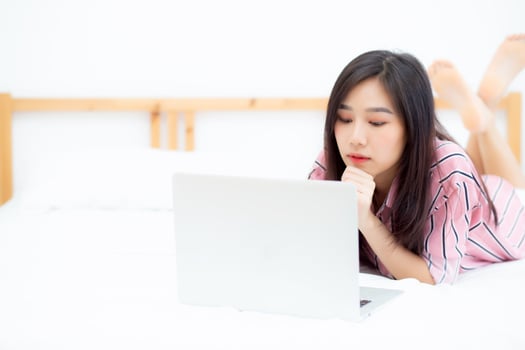Beautiful asian young woman lying on bed using laptop at bedroom for leisure and relax, freelance with girl working notebook, communication concept. photo