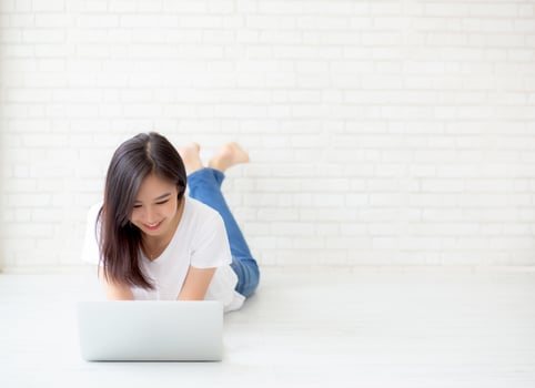 Young asian woman working online laptop lying on floor brick cement background, freelance girl using notebook computer with connect to internet for distance job, business and lifestyle concept. photo