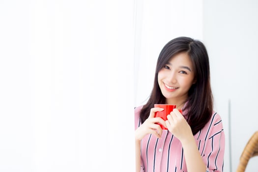 Beautiful of portrait young asian woman with drink a cup of coffee standing curtain window background in bedroom, girl relax in morning at home, lifestyle concept. photo