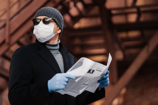 Virus spread and quarantine concept. Serious man wears sunglasses, hygienic mask and rubber gloves, looks away, reads press, protects himself from risk of viral disease or coronavirus, air pollution photo
