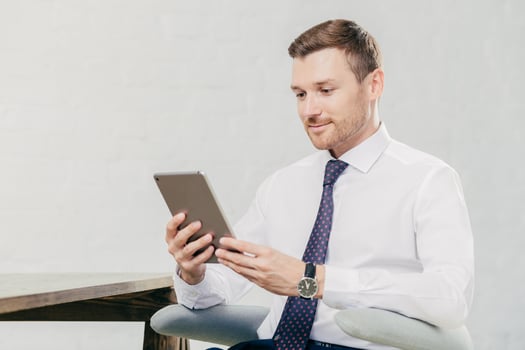 Male executive manager in white shirt and tie, holds tablet computer, searches necessary information in internet, connected to wifi in office. People, business and modern technologies concept photo