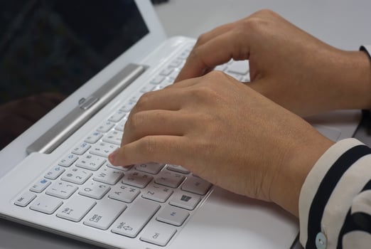woman sitting at desk typing on the keyboard of a white laptop photo