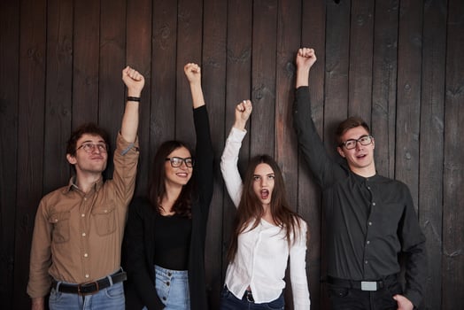 Girl in white shirt screaming. Celebrating succeess. Friends put their hands up against black wooden wall photo