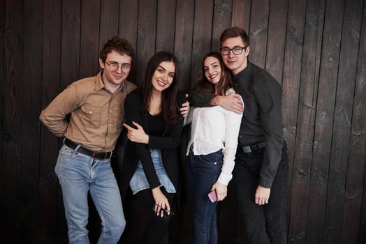 Satisfied young people. Youth stands against black wooden wall. Group of friends spending time together photo