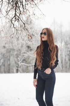 Alone in the park. Pretty girl with long hair in black blouse and eyewear is in the winter forest photo