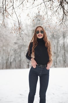 In the eyewear. Pretty girl with long hair in black blouse and eyewear is in the winter forest photo