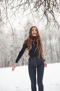 Slim body type. Pretty girl with long hair and in black blouse dancing in the winter forest photo