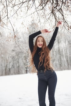 With hands up. Pretty girl with long hair and in black blouse dancing in the winter forest photo