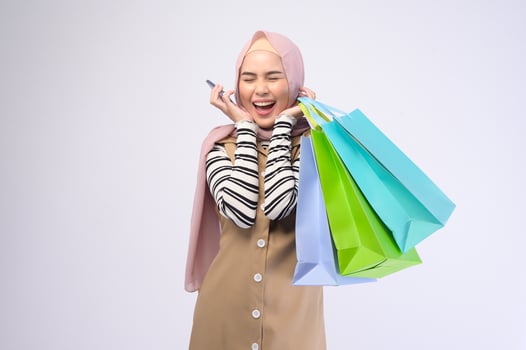 Young beautiful muslim woman in suit holding colorful shopping bags over white background studio photo