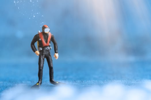 Miniature people Scuba Diver standing underwater with blue background photo