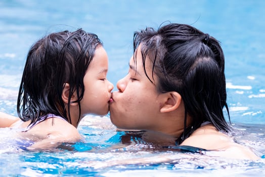 Portrait of mother and daughter are kissing. Image of Asian family showing love and bonding. Women and little girl are playing in water pool at resort. In summer time. Children 4-5 years old. photo