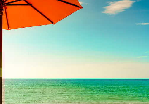 Orange beach umbrella on golden sand beach by the sea with emerald green sea water and blue sky and white clouds. Summer vacation on tropical paradise beach concept. Skyline between sea and sky. photo
