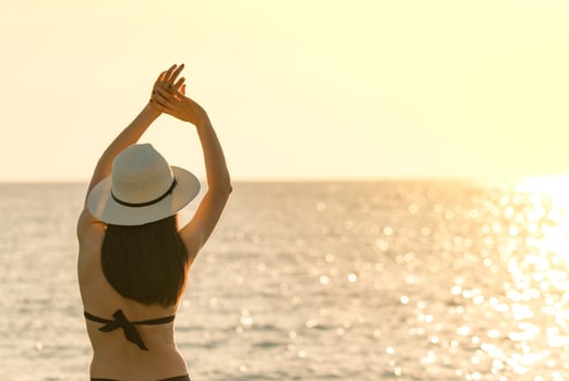 Back view of happy young Asian woman in black swimsuit and straw hat relax and enjoy holiday at tropical paradise beach at sunset. Girl in summer vacation fashion. Beauty sexy model. Elegant lifestyle photo