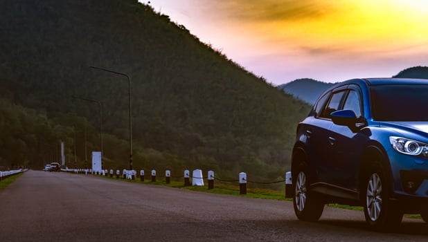 Blue SUV car parked on asphalt road in front of the mountain. Car parked at the park in early morning with sunrise sky. Road trip travel. Car parking space. Automotive industry. Nature tourism. photo