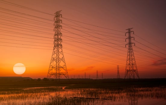 High voltage electric pylon and electrical wire with sunset sky. Electricity poles. Power and energy concept. High voltage grid tower with wire cable. Beautiful big sun at sunset  with red-orange sky. photo