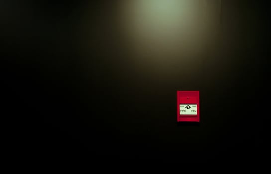 Red fire alarm pull station on black wall background. Fire alarm switch. Emergency safety system. Fire alarm on dark concrete wall. Warning and security system. Red box for safety alert on wall. photo