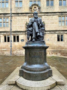 A statue of a man sitting on a chair in front of a building photo