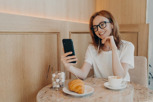 Beautiful redhead woman in earphones sitting in cafe and making video call on mobile phone photo